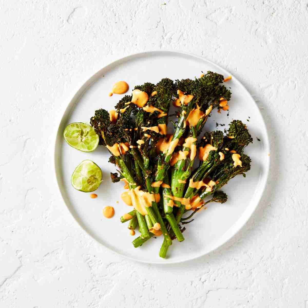 A plate with air fried broccolini drizzled with chipotle mayo. 