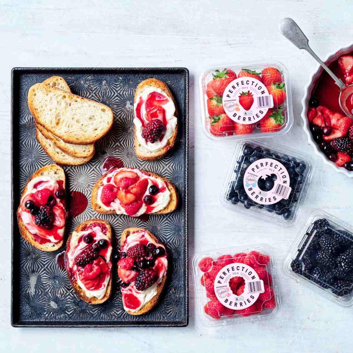 Toast topped with yoghurt, and roasted berries on a baking tray with punnets of berries next to it.