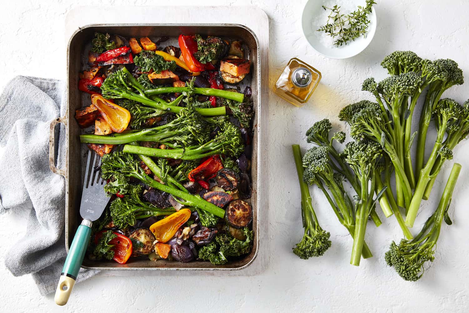 Roasted vegetables in a roasting tray with broccolini next to the tray.