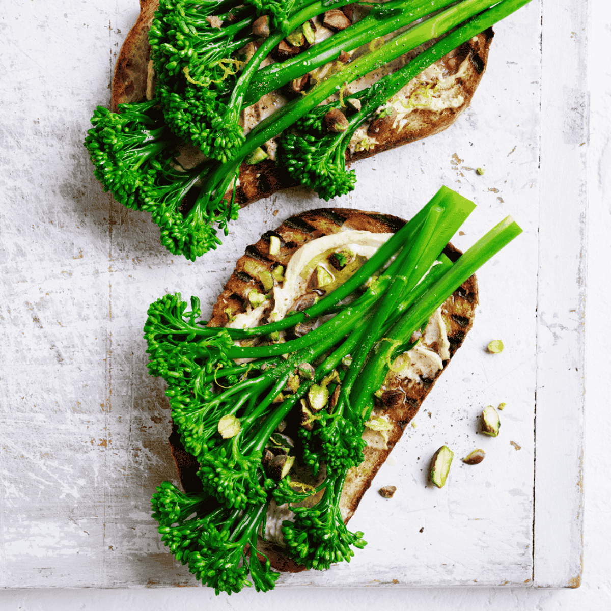 Two pieces of toasted bread, topped with hummus and Broccolini