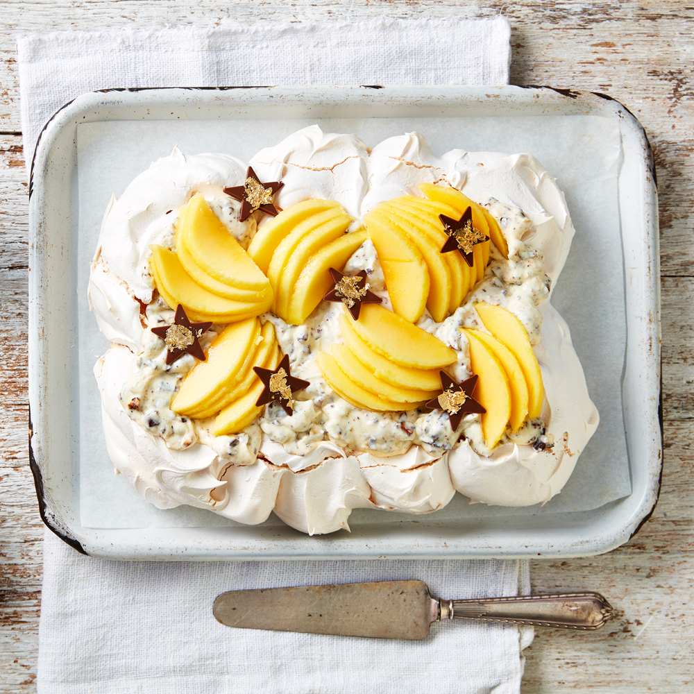 Pavlova on a baking tray topped with cannoli cream, and sliced Calypso mangoes.
