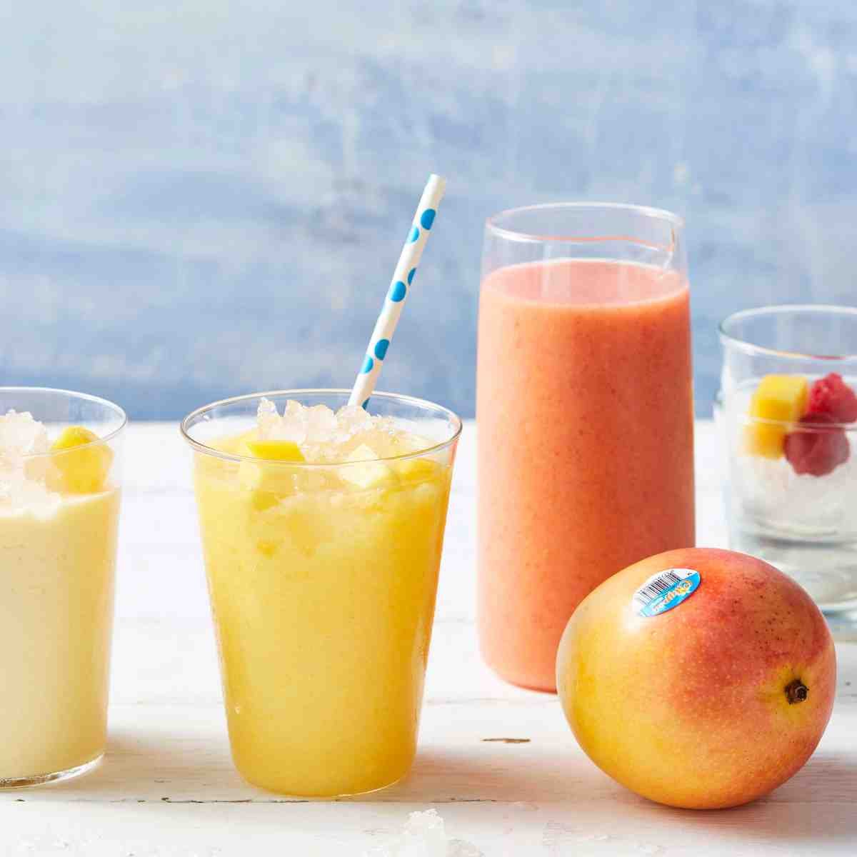 Three glasses filled with mango ginger smoothie, with a mango placed next to the glasses.