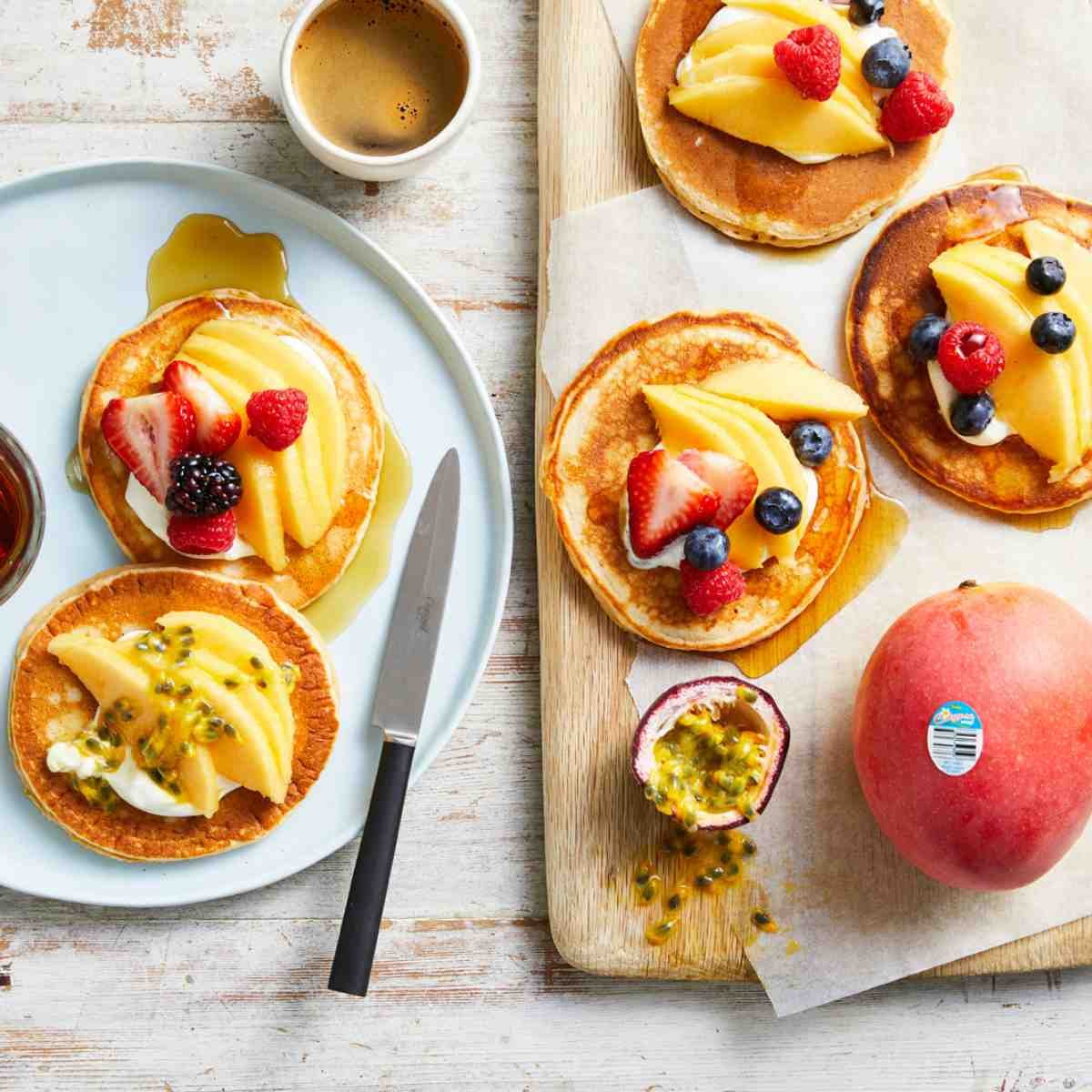 Stacks of pancakes topped with yoghurt, and various fruit such as blackberries, mangoes, blueberries, passionfruit and strawberries.