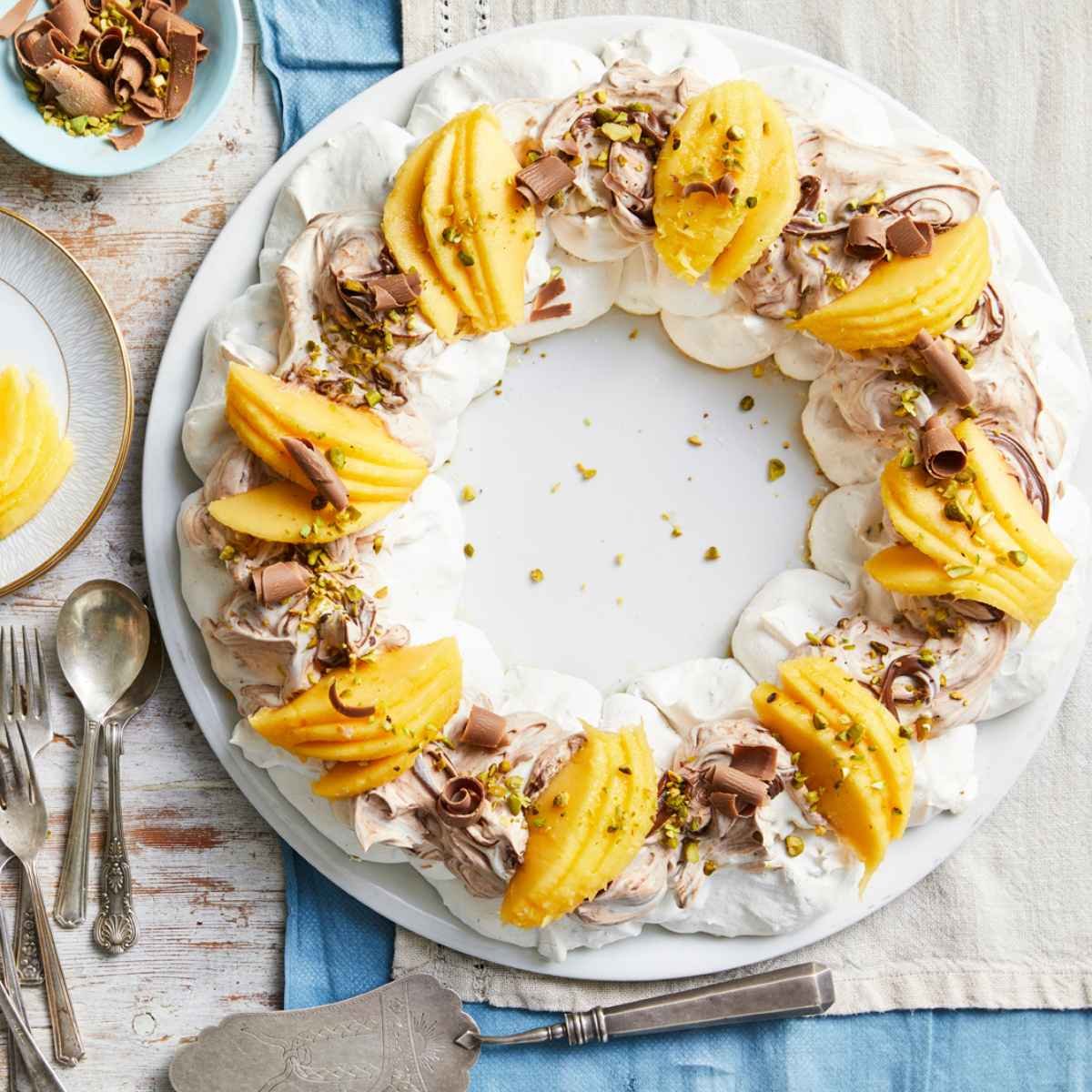 A holiday wreath on a plate with pavlova, topped with hazlenut cream and Calypso mangoes, drizzled with pistachios.