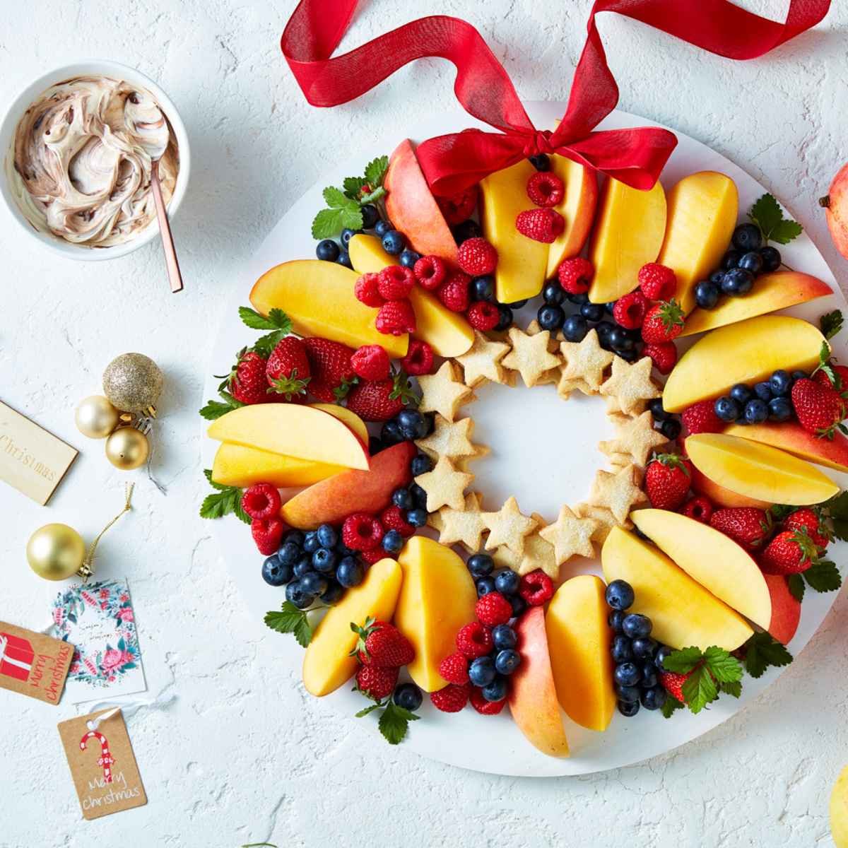 A white plate topped with a fruit wreath made out of Calypso mangoes, berries and biscuits.