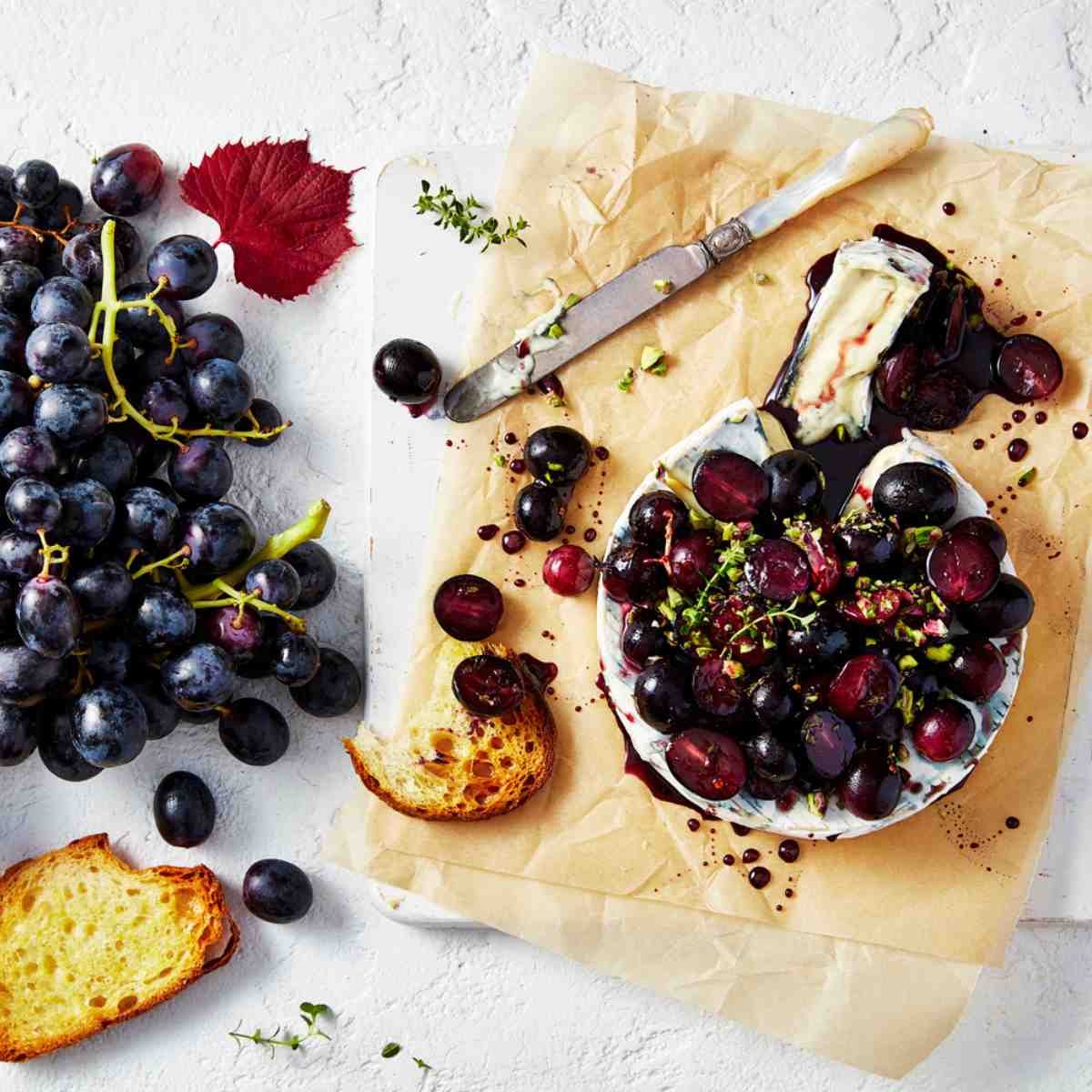A round of brie topped with grapes, chili flakes and honey with more grapes on the side.