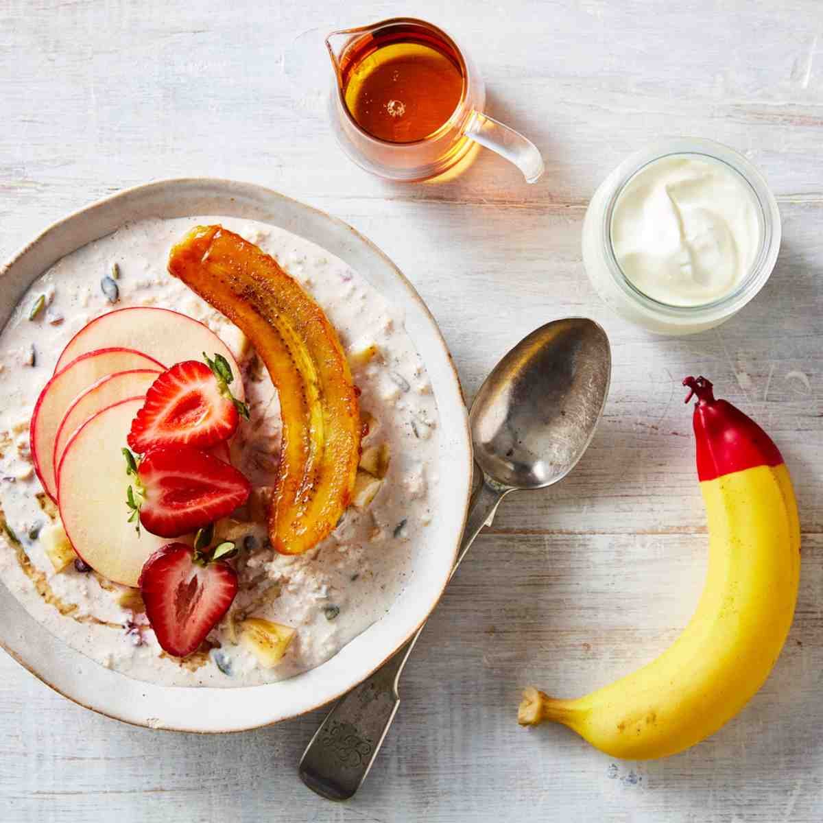 A bowl of oatmeal topped with apples, strawberries and bananas.