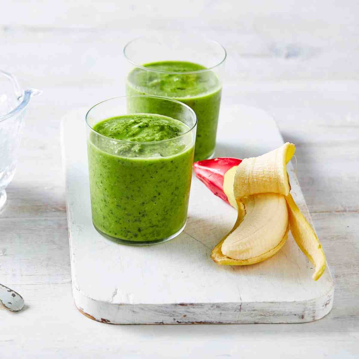 Two glasses of green banana smoothie placed on a chopping board.