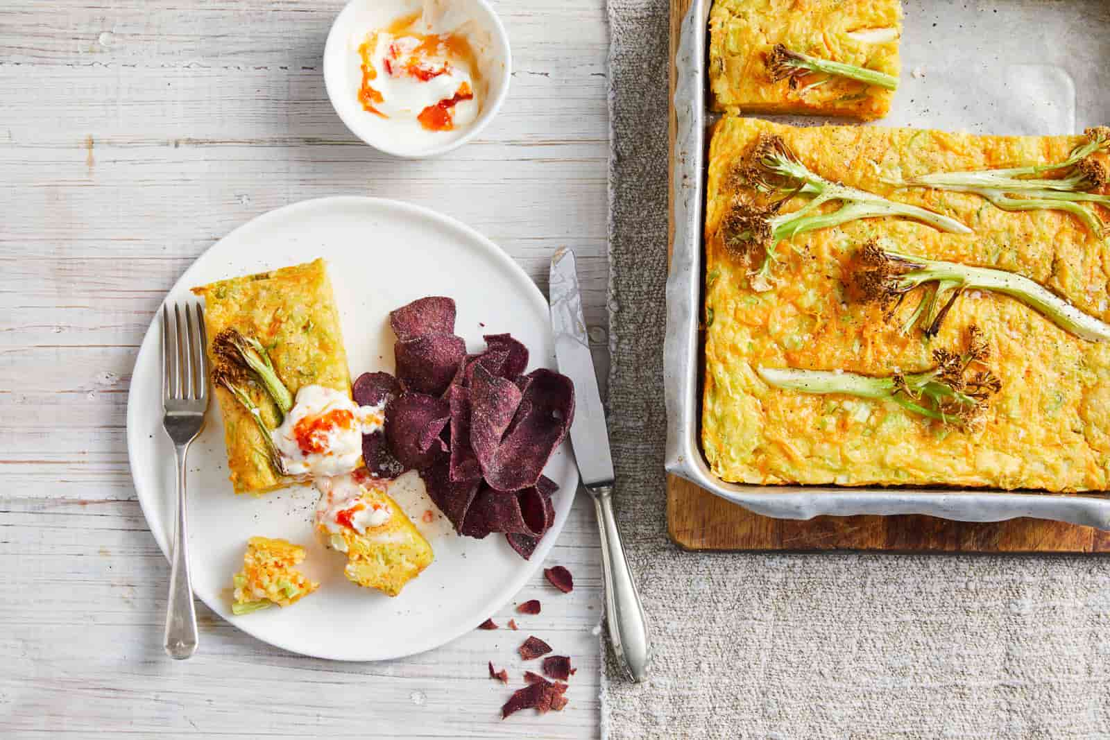 Carrot, halloumi and cauli-blossom slice in a baking tray, with a slice on a plate next to it.