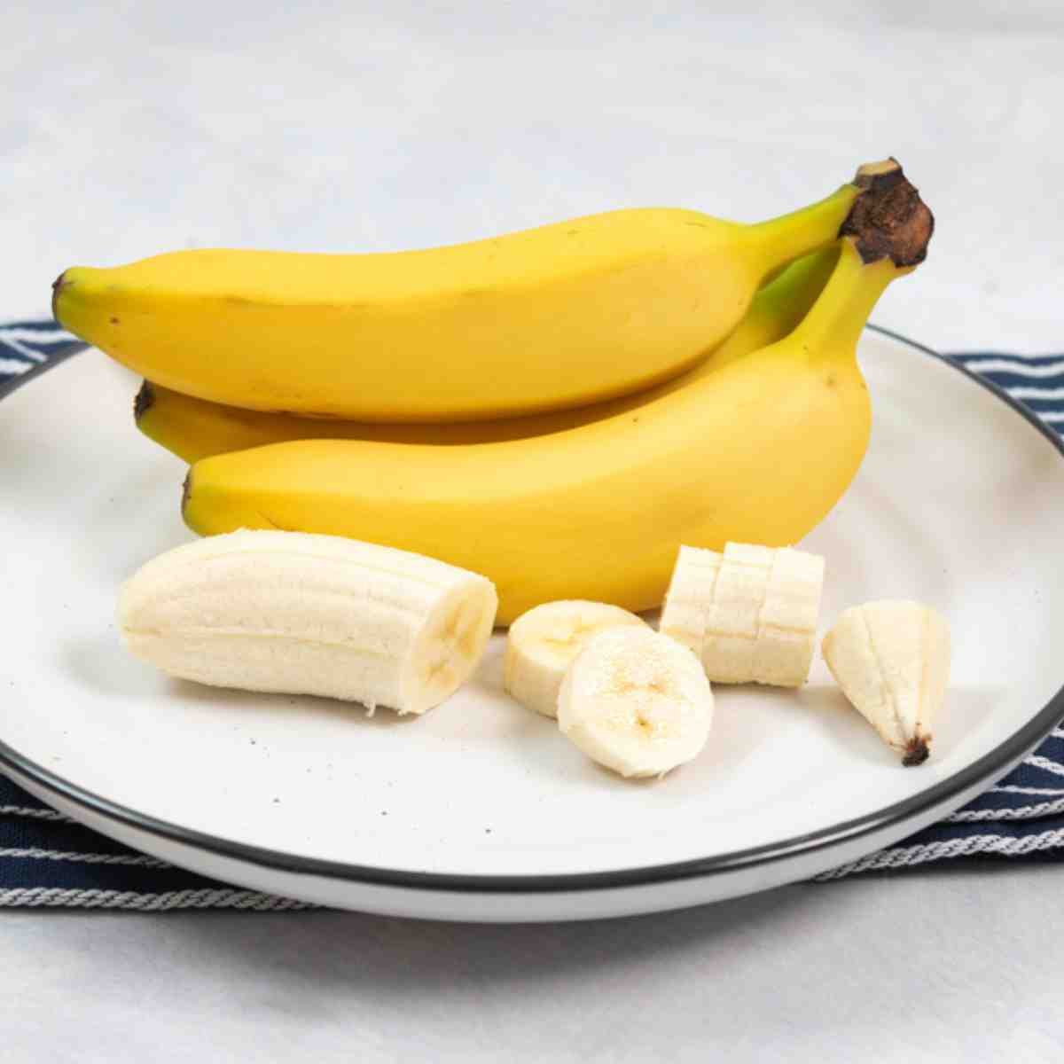 A plate with a bunch of Havana bananas, along with one sliced banana.