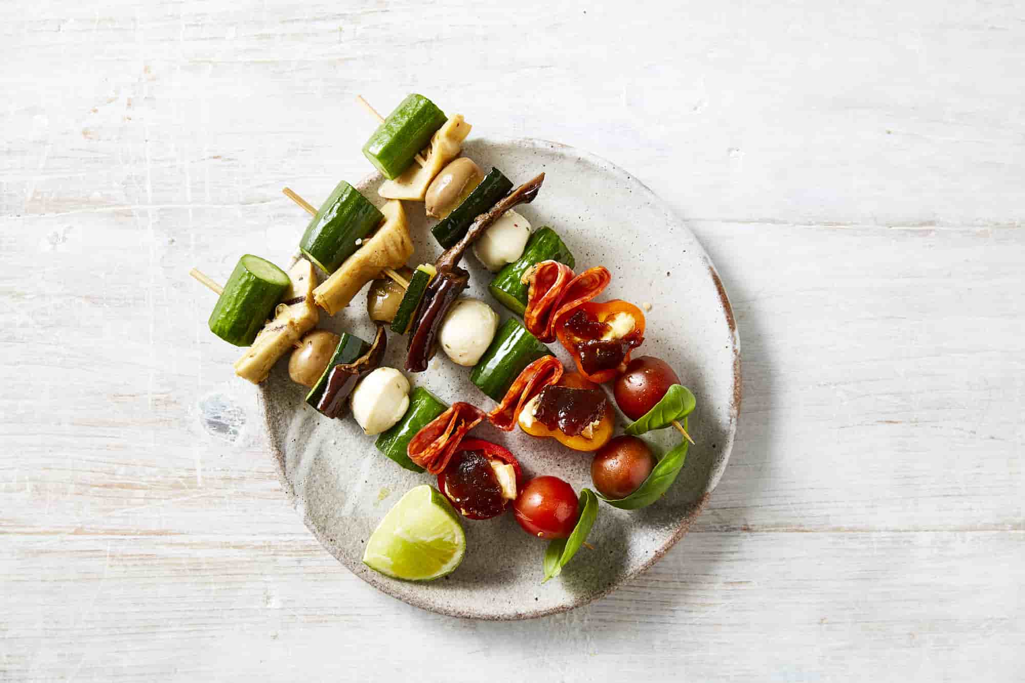 Antipasto on skewers with charcuterie, cucumbers and tomatoes placed on a plate.