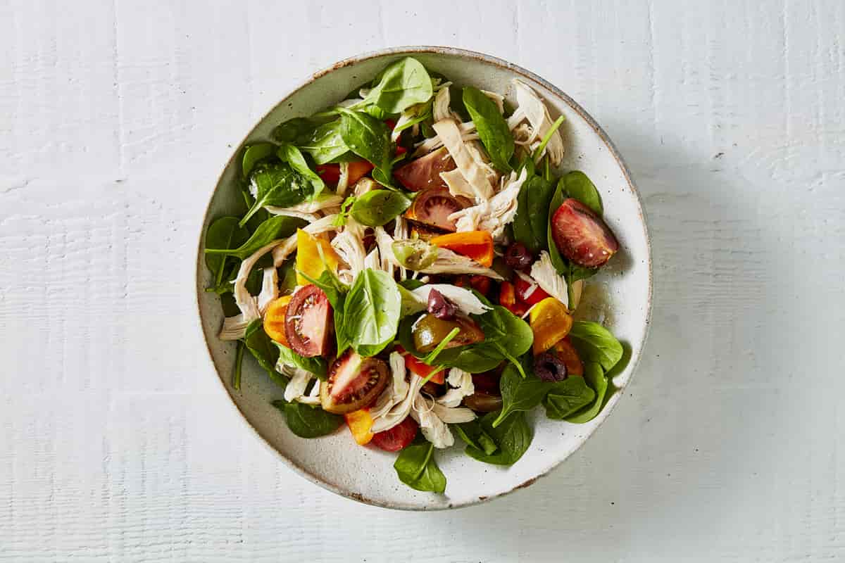 A bowl with tomato wedges, lettuce, chicken and olives.