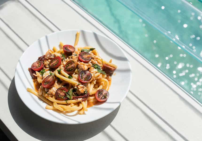 Bucatini pasta topped with fresh Kumato tomato in a white bowl.