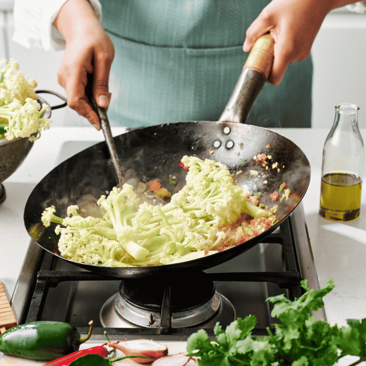 A person stir frying cauliblossom in a Wok. You can only see the hands and wok close up.