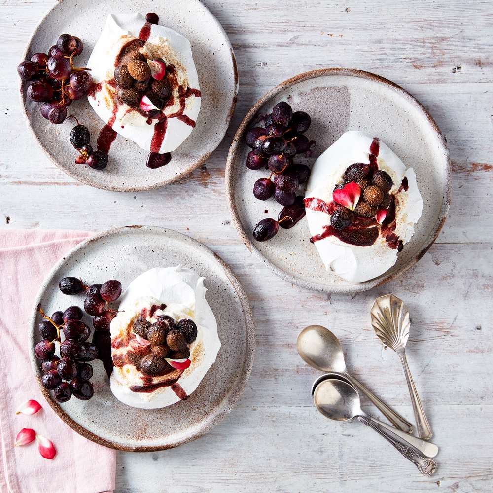 Three plates with mini pavlovas topped with roasted grapes, and more grapes on the side.