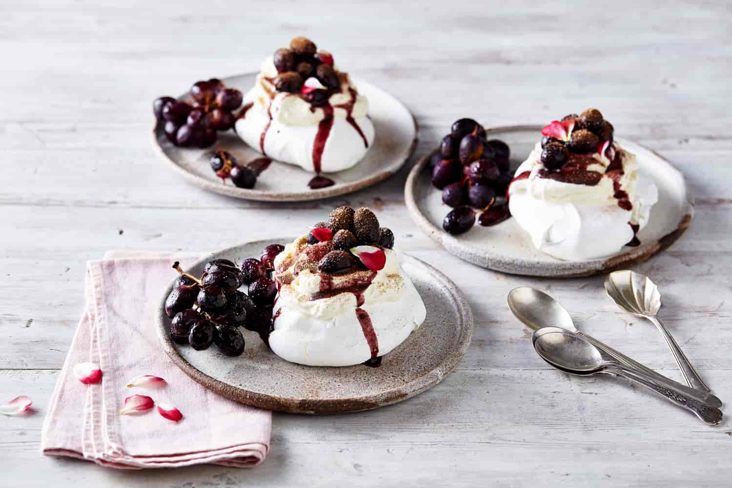 Three plates with mini pavlovas topped with roasted grapes.