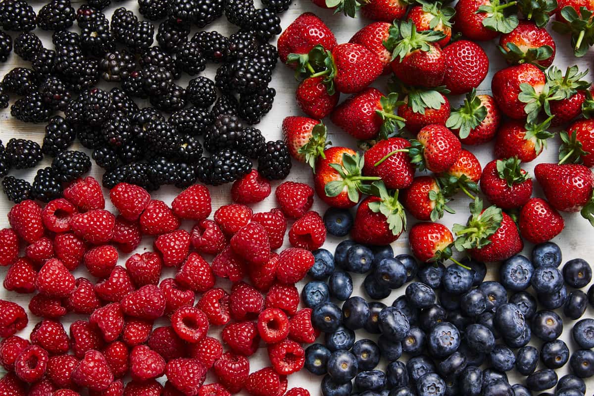 Strawberries, blueberries, blackberries and raspberries on a wooden board.