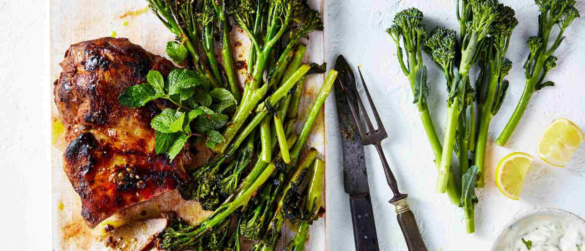 Roasted broccolini with oven roasted lamb, topped with mint leaves on a white serving board.