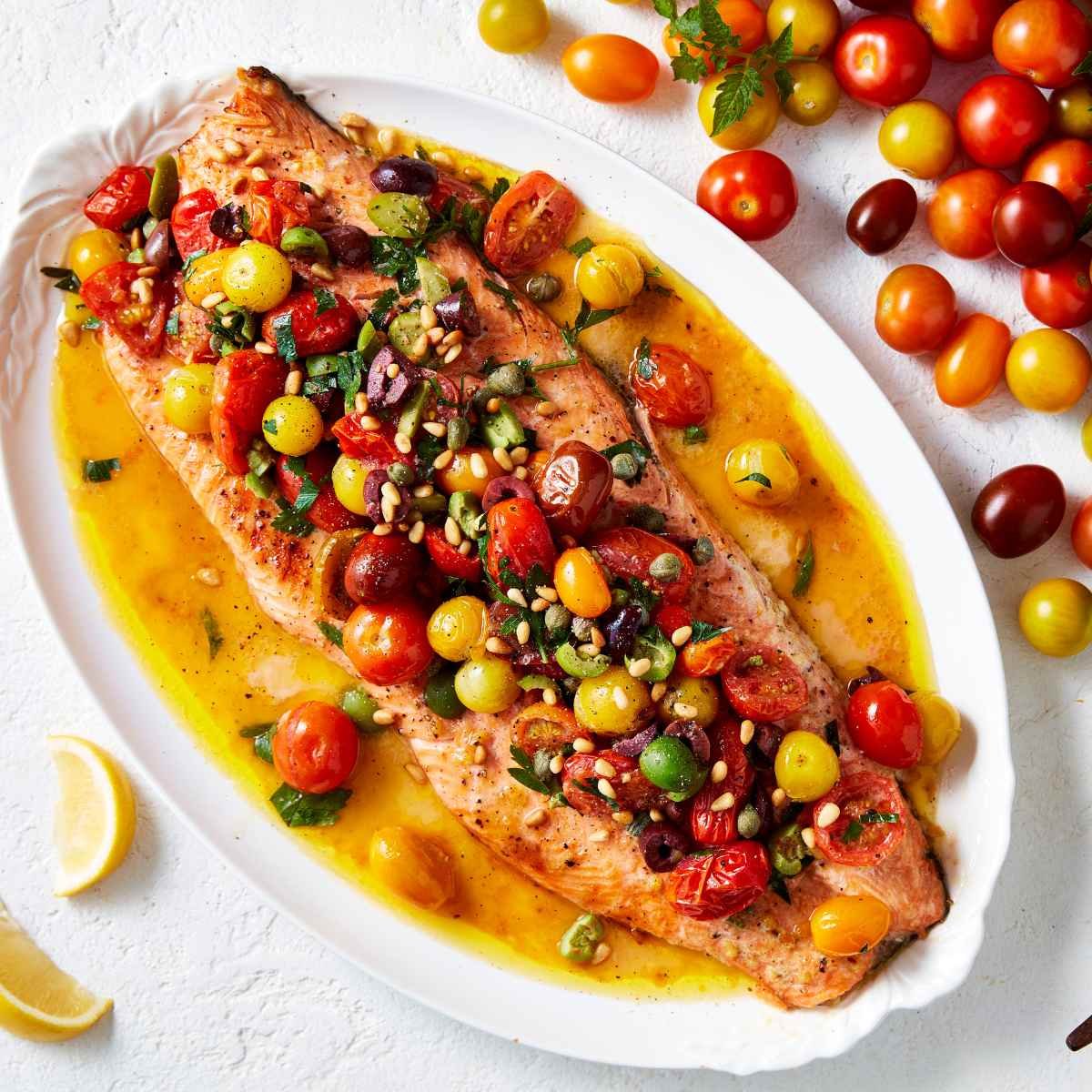 Whole side of salmon on a white platter with medley Mix-a-Mato tomatoes on top. 