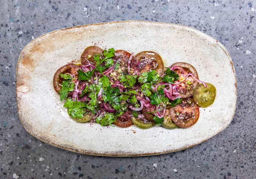 Tomato salad topped with herbs on a white platter.