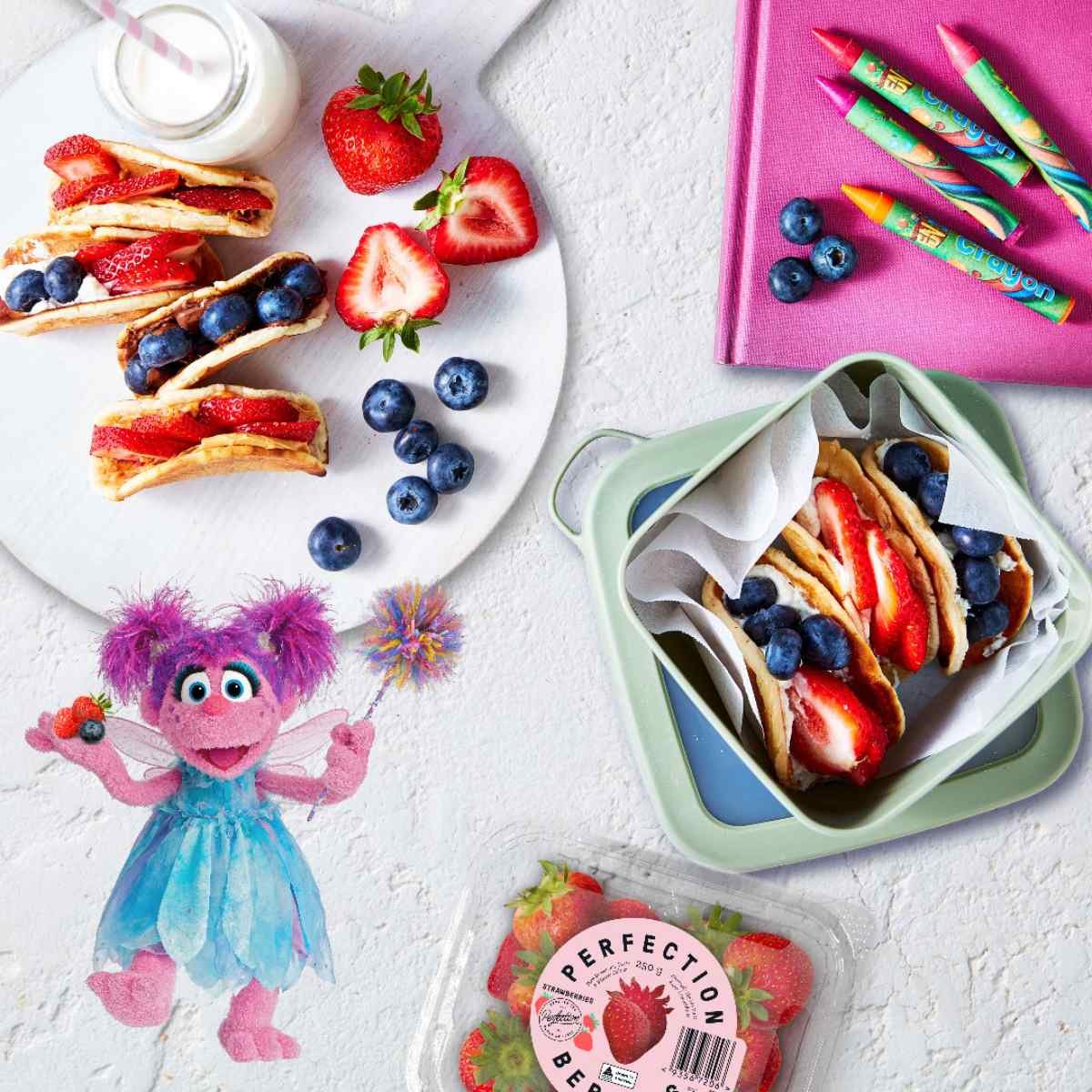 Taco pikelets filled with blueberries, strawberries, and cream on a plate and in a lunchbox. 