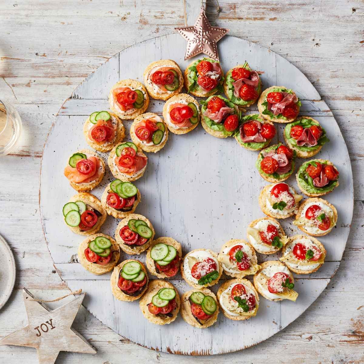 A wreath made out of scones, topped with solanato tomatoes, and qukes cucumbers on a white board.