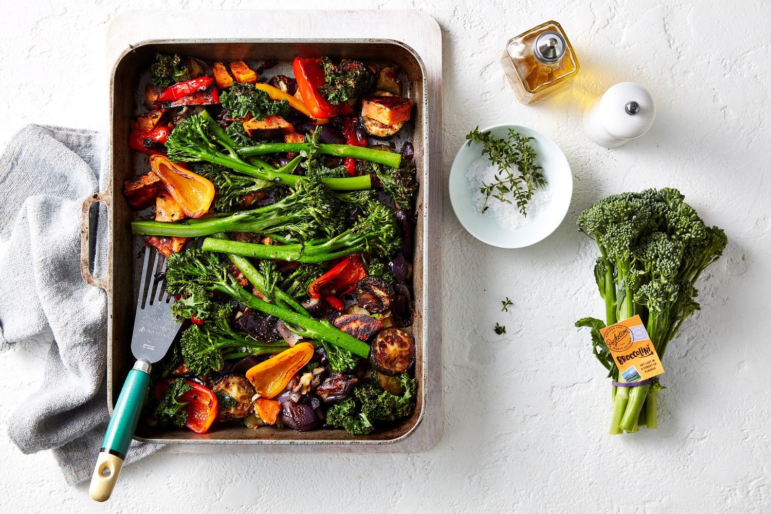 A roasting tray with roasted vegetables that include Broccolini, mini capsicums, onion, zucchini.
