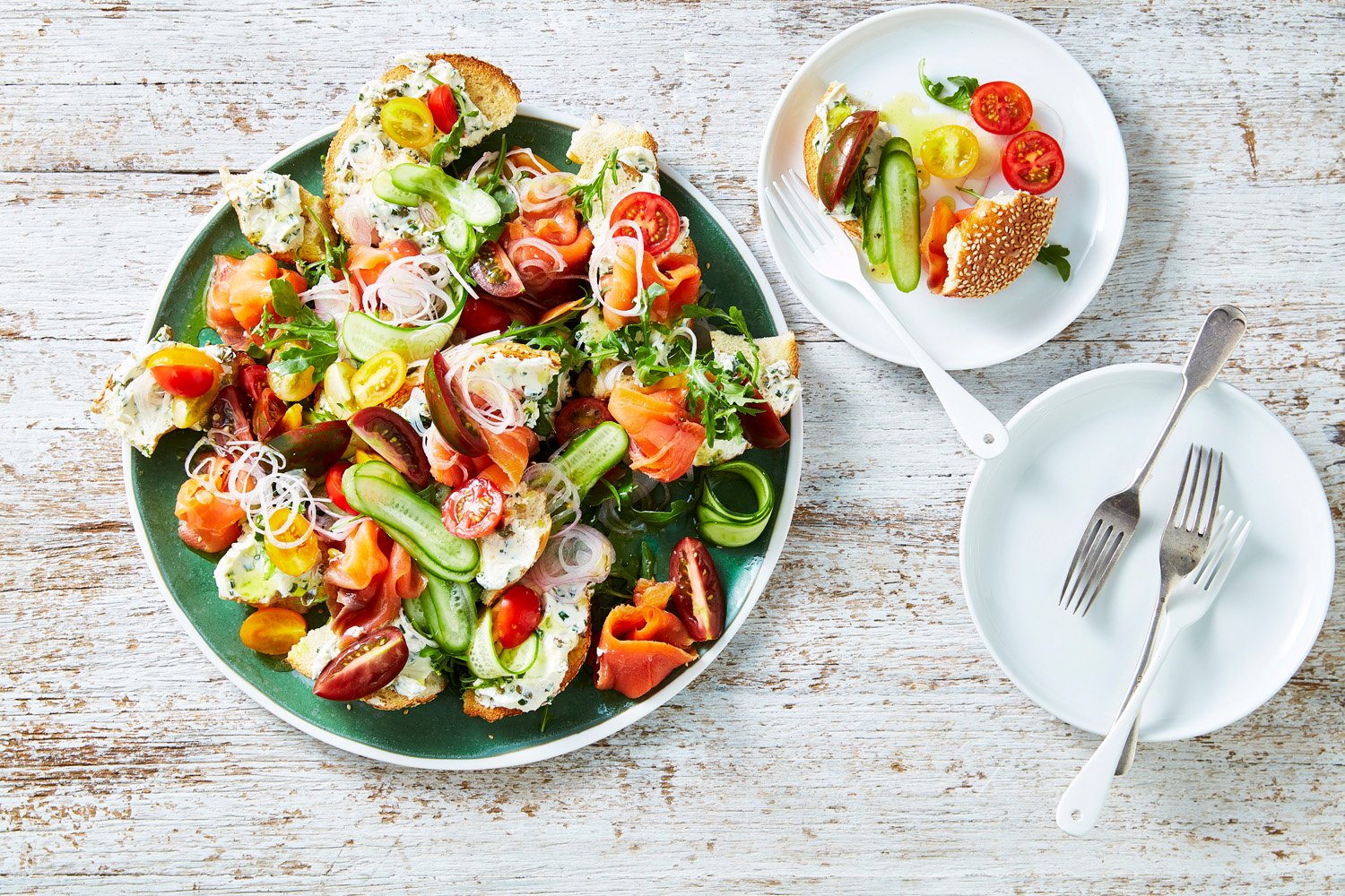 A plate with a salad of tomatoes, cucumbers, smoked salmon and bagels.