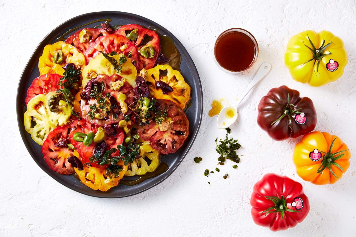 Sliced Monterosa tomatoes in different colours on a black plate with dressing on top.