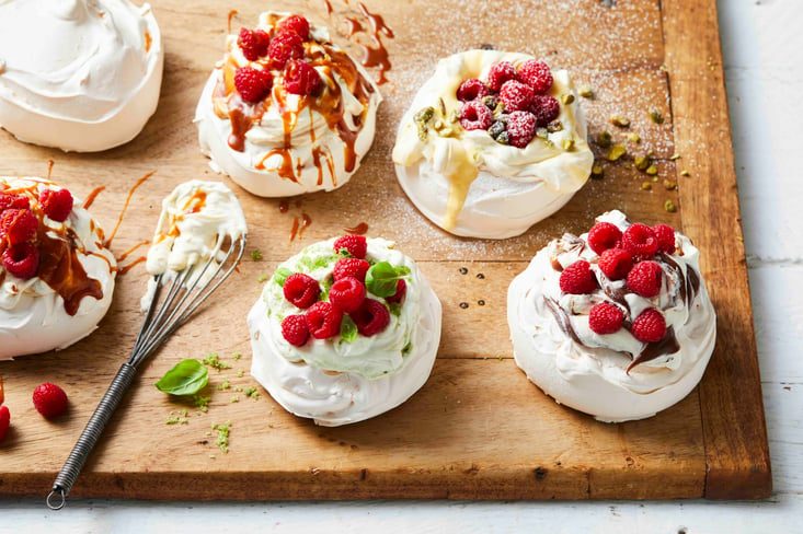 Individual pavlovas topped with cream on a wooden serving board.