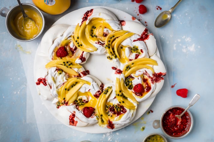 A pavlova wreath topped with sliced mango, passionfruit and raspberries.