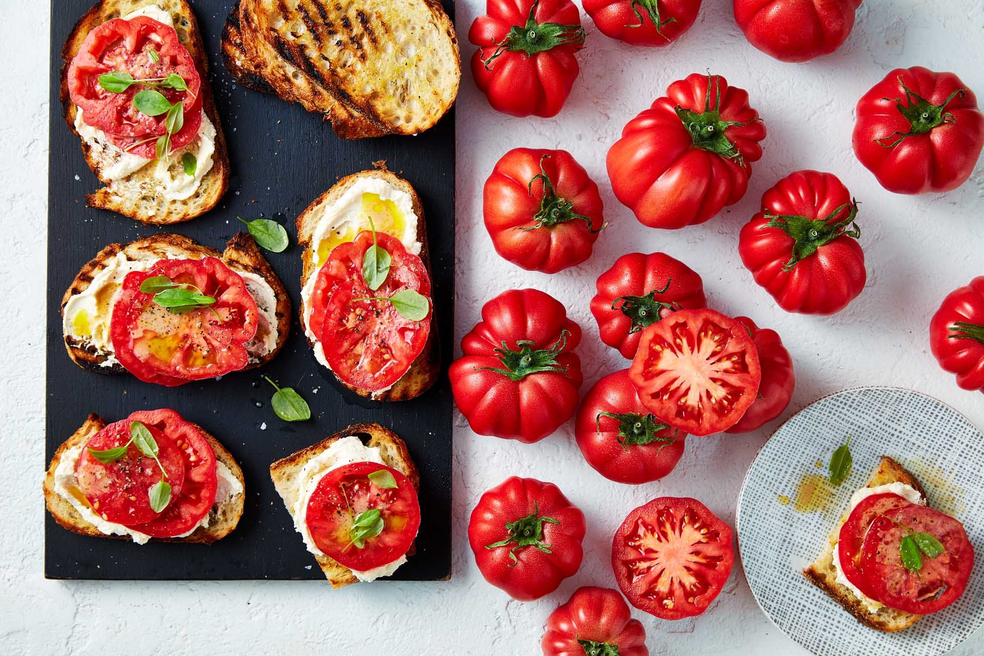 Toasted bread with cream cheese, and sliced monterosa tomates on top with basil.