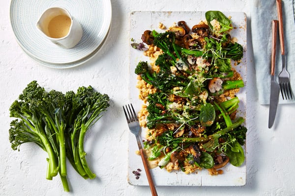 Smashed chickpeas topped with broccolini and salad leaves on a white platter.