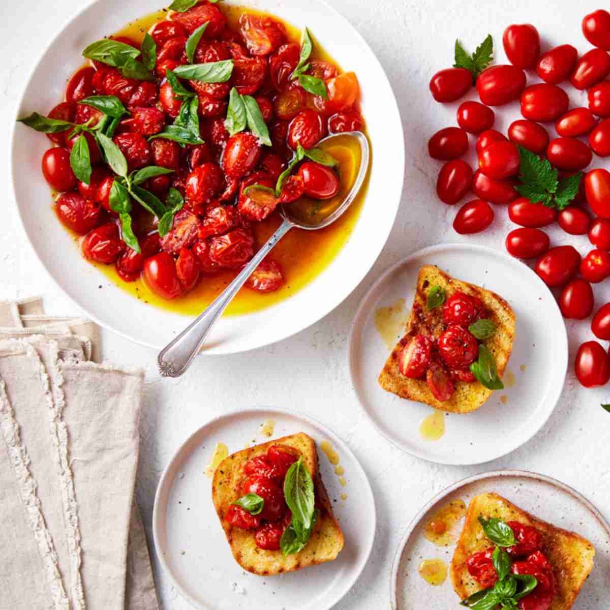 Three plates of garlic bread bruschetta topped with roasted solanato tomatoes and basil. Plus a plate of roasted tomatoes on the side.