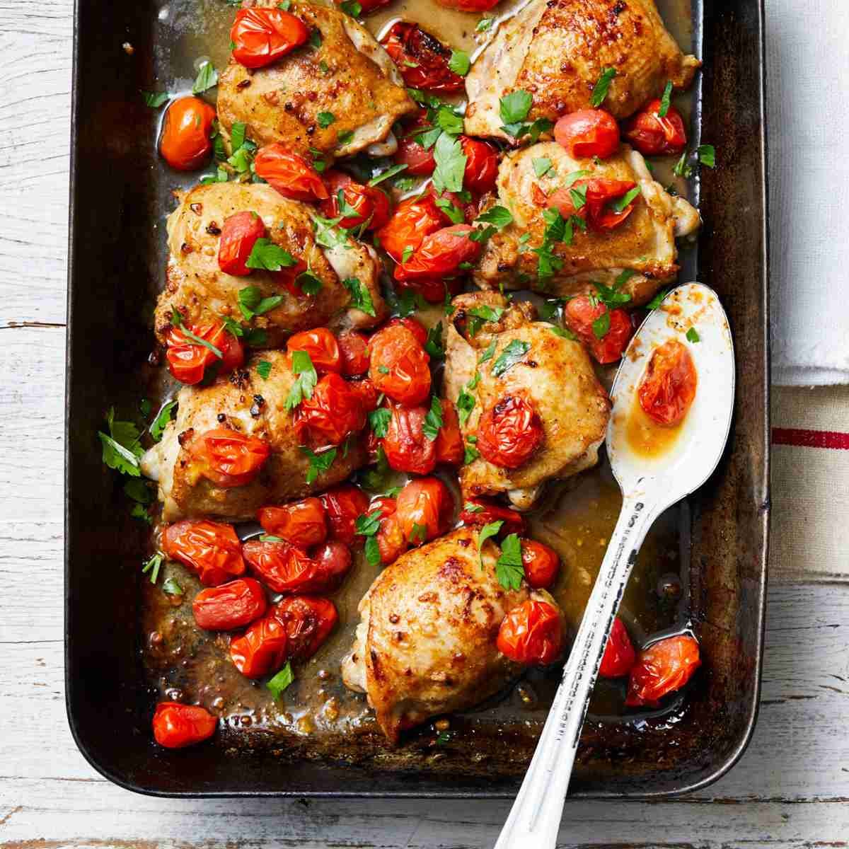A baking tray with roasted chicken, solanato tomatoes, and herbs sprinkled on top with a spoon. https://www.perfection.com.au/recipes/roast-solanato-tomato-and-mustard-chicken-with-french-fries?hsLang=en-au 