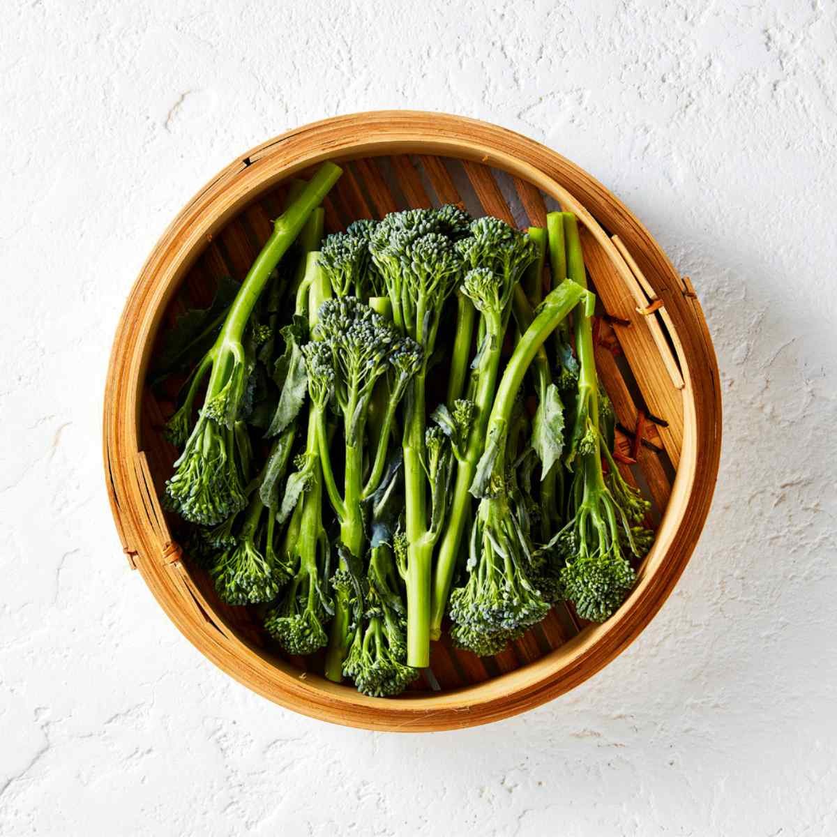 Raw Broccolini in a wooden steamer basket. 