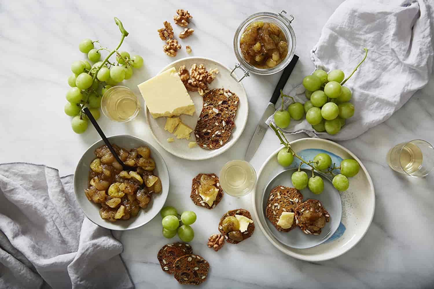 A bowl of grape chutney with crackers, and green grapes around it.